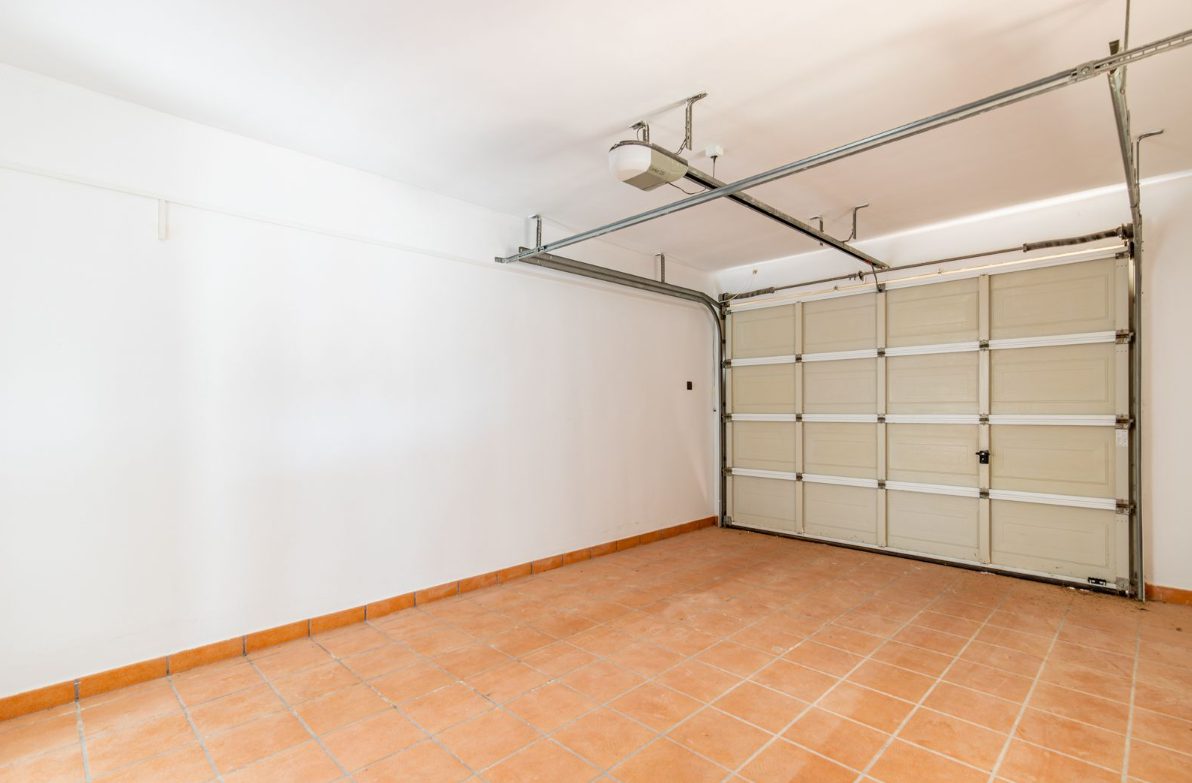 A garage with a closed door and tiled floor of a 5-bedroom villa in Benitachell - The Estates