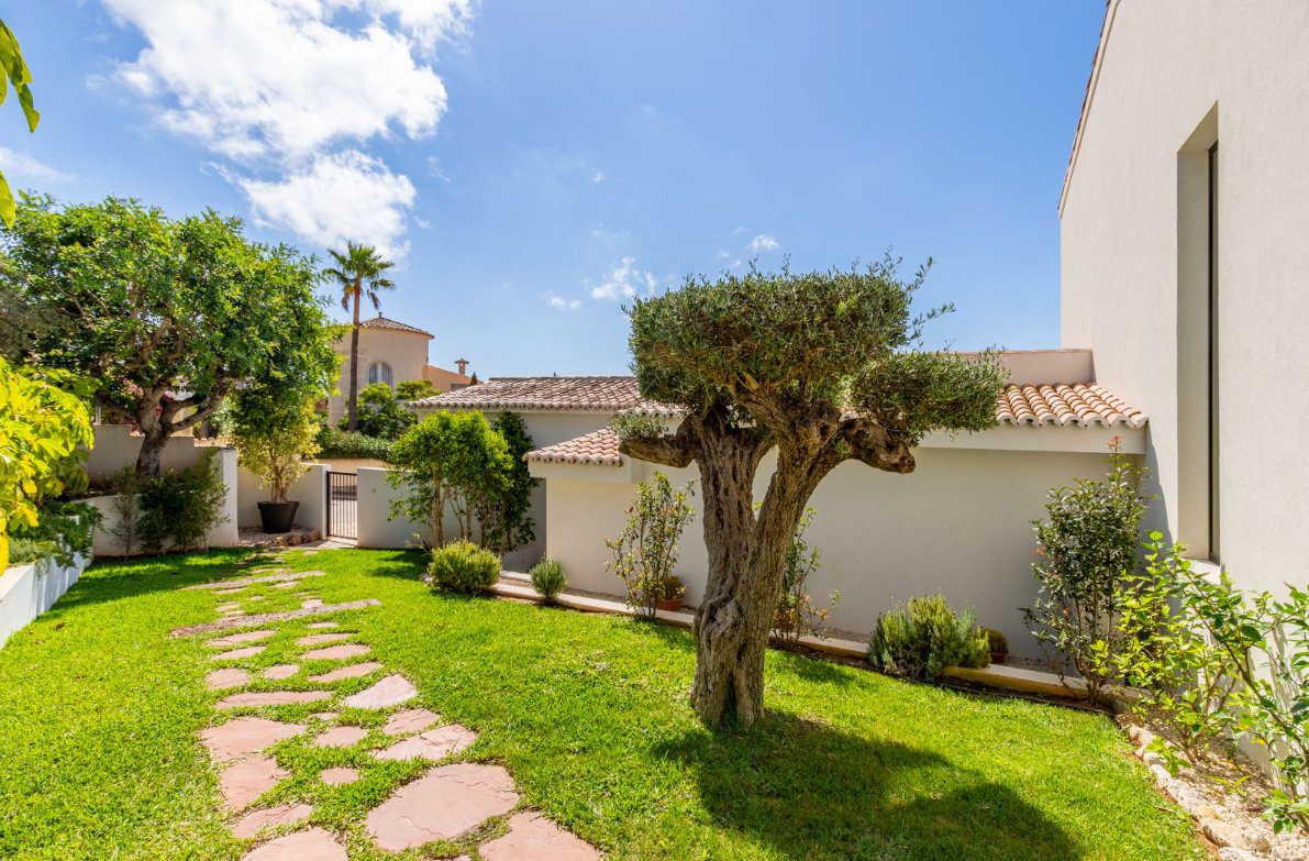 A lush garden with a stone path and mature tree at a 5-bedroom villa in Benitachell - The Estates