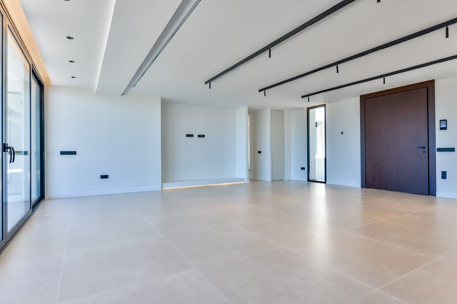 Modern minimalist living area with floor-to-ceiling windows, tiled floors and dark ceiling beams in a 4-bedroom villa in Altea - The Estates