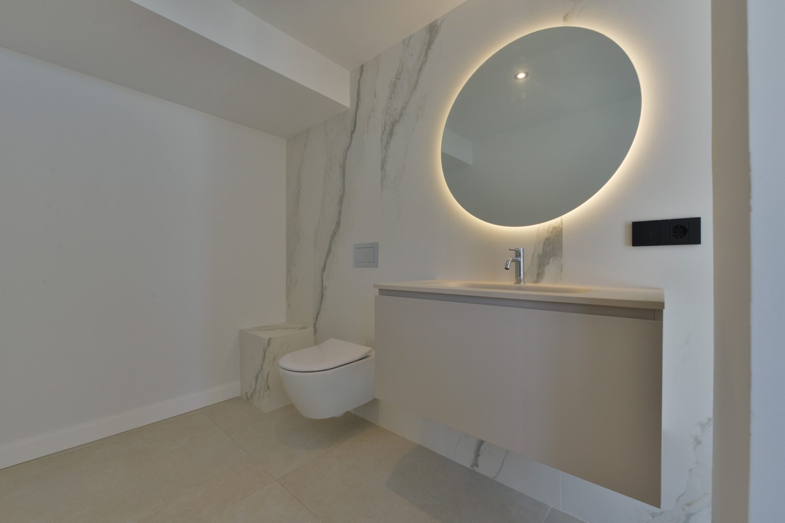 Modern bathroom with marble-effect walls, floating vanity, wall-mounted toilet and illuminated round mirror in a 4-bedroom villa in Altea - The Estates