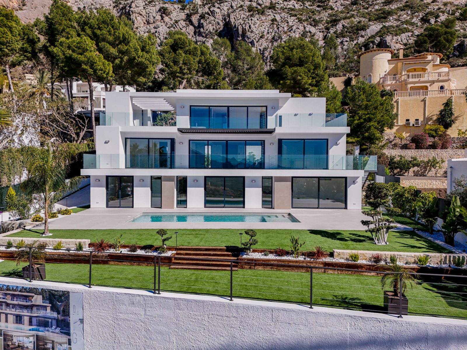 Modern white villa facade with swimming pool, landscaped garden and mountain backdrop in Altea - The Estates