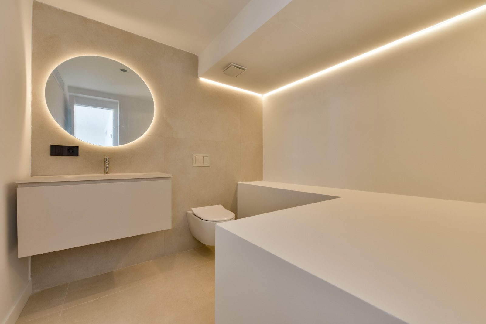 Modern bathroom with illuminated round mirror, wall-mounted vanity and bathtub of a 4-bedroom