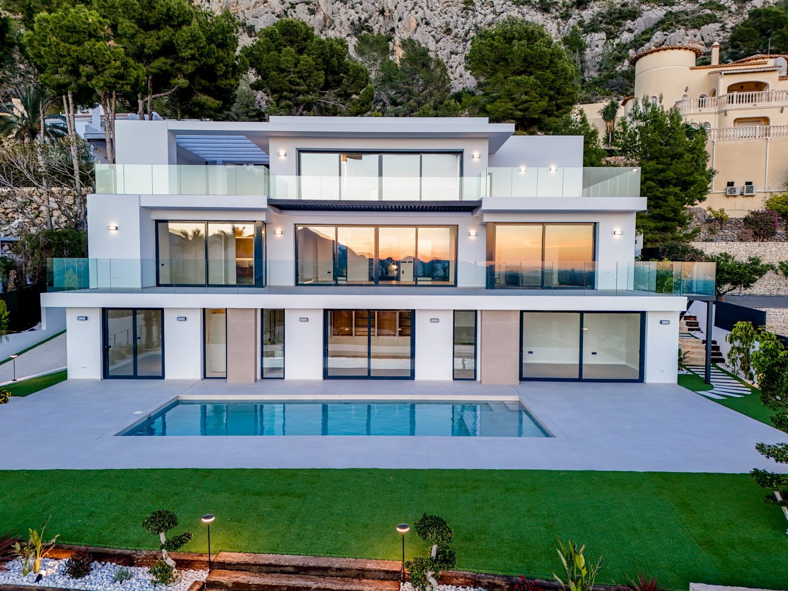 Modern villa with glass balconies, pool and landscaped garden against a mountain backdrop in Altea - The Estates