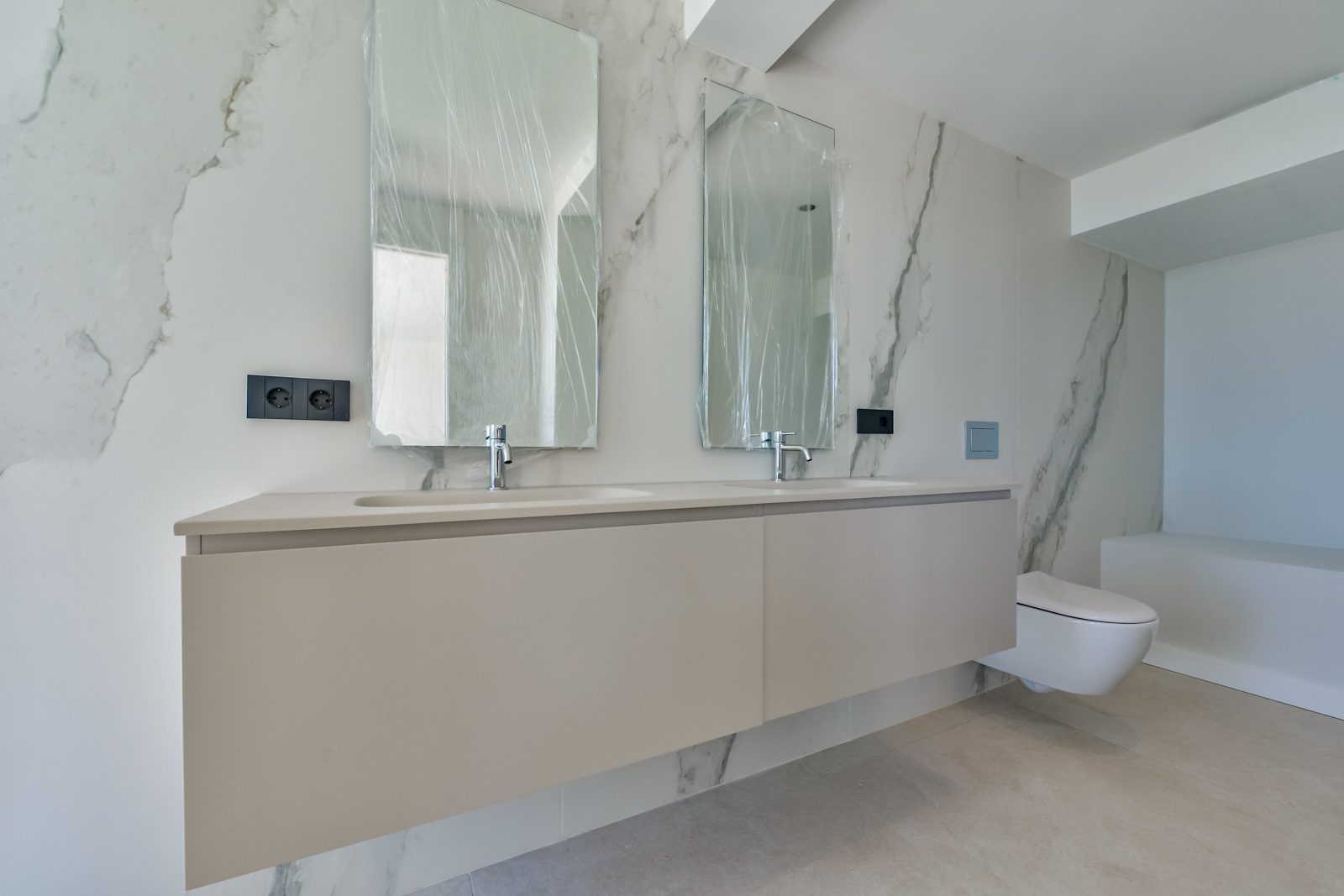 Modern marble bathroom with double vanity, mirrors, wall-hung toilet and bathtub in a 4-bedroom villa in Altea - The Estates