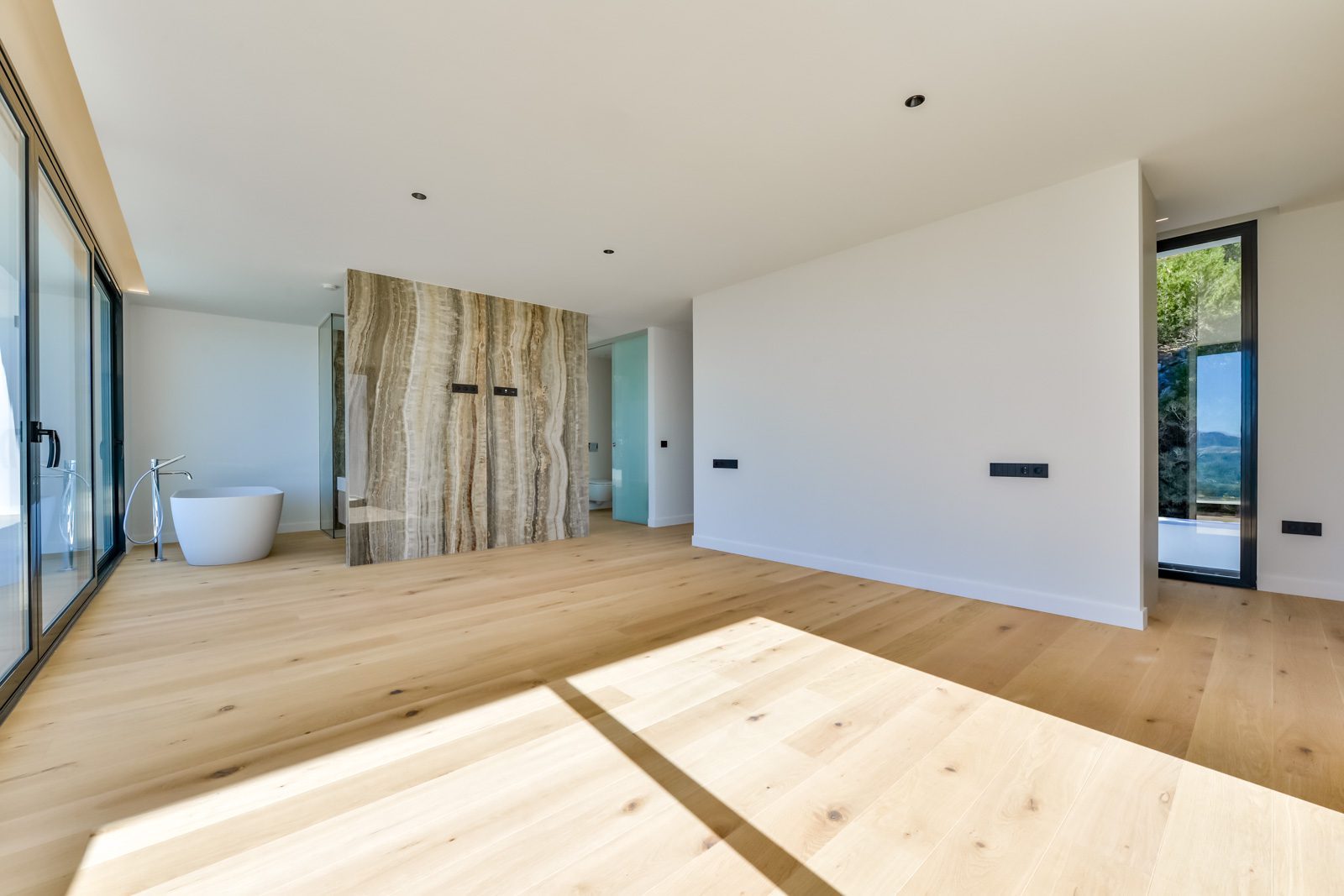 Modern bedroom with freestanding bathtub, stone feature wall and panoramic windows in a 4-bedroom villa in Altea - The Estates