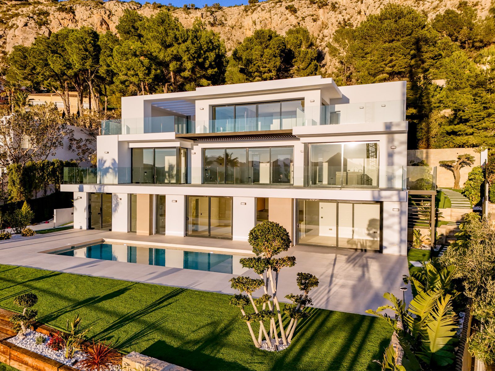 Modern white villa with pool and landscaped gardens against a mountain backdrop of a