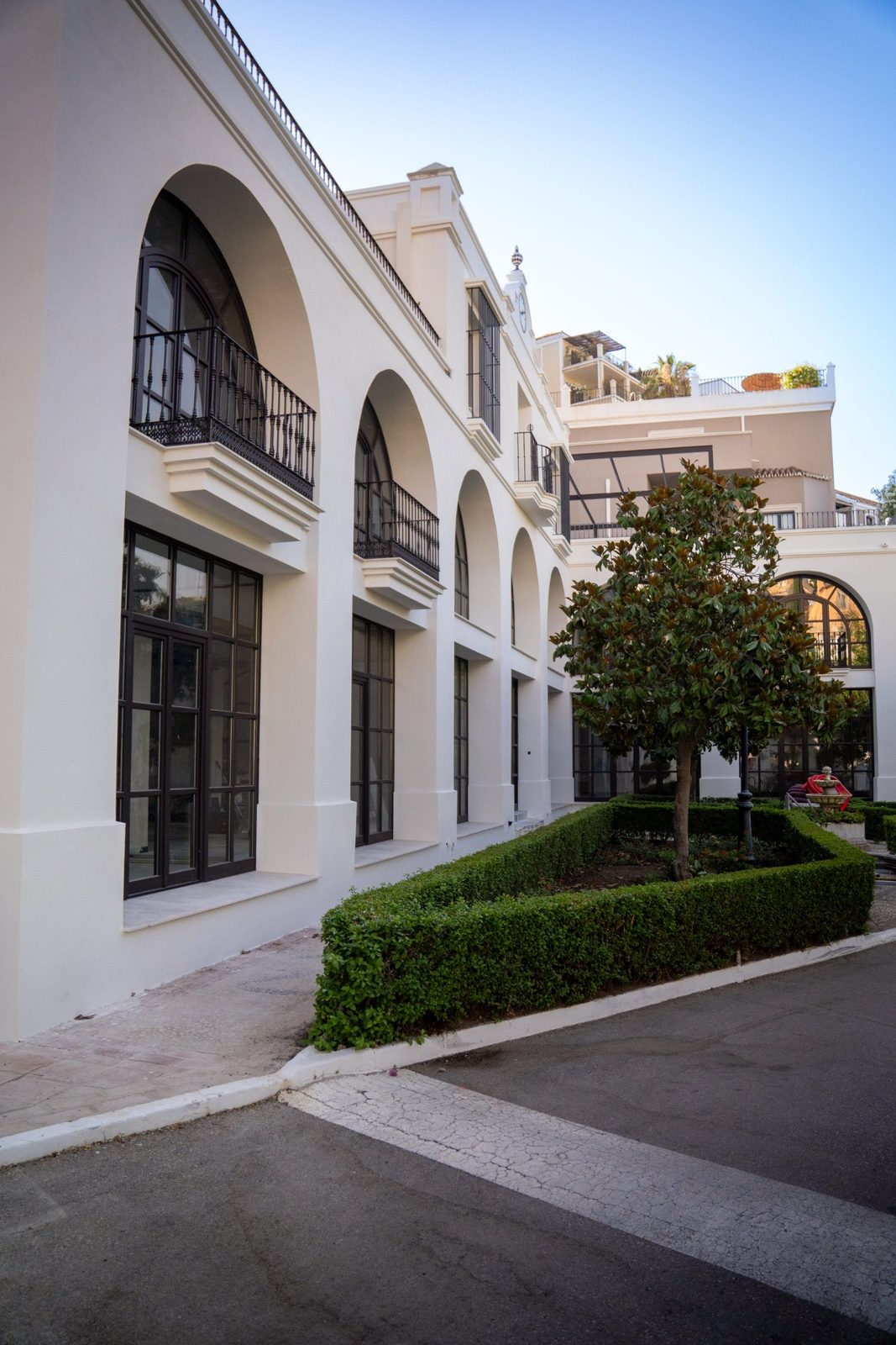 Elegant white courtyard facade with arched windows, balconies and manicured hedges at a property in Málaga - The Estates