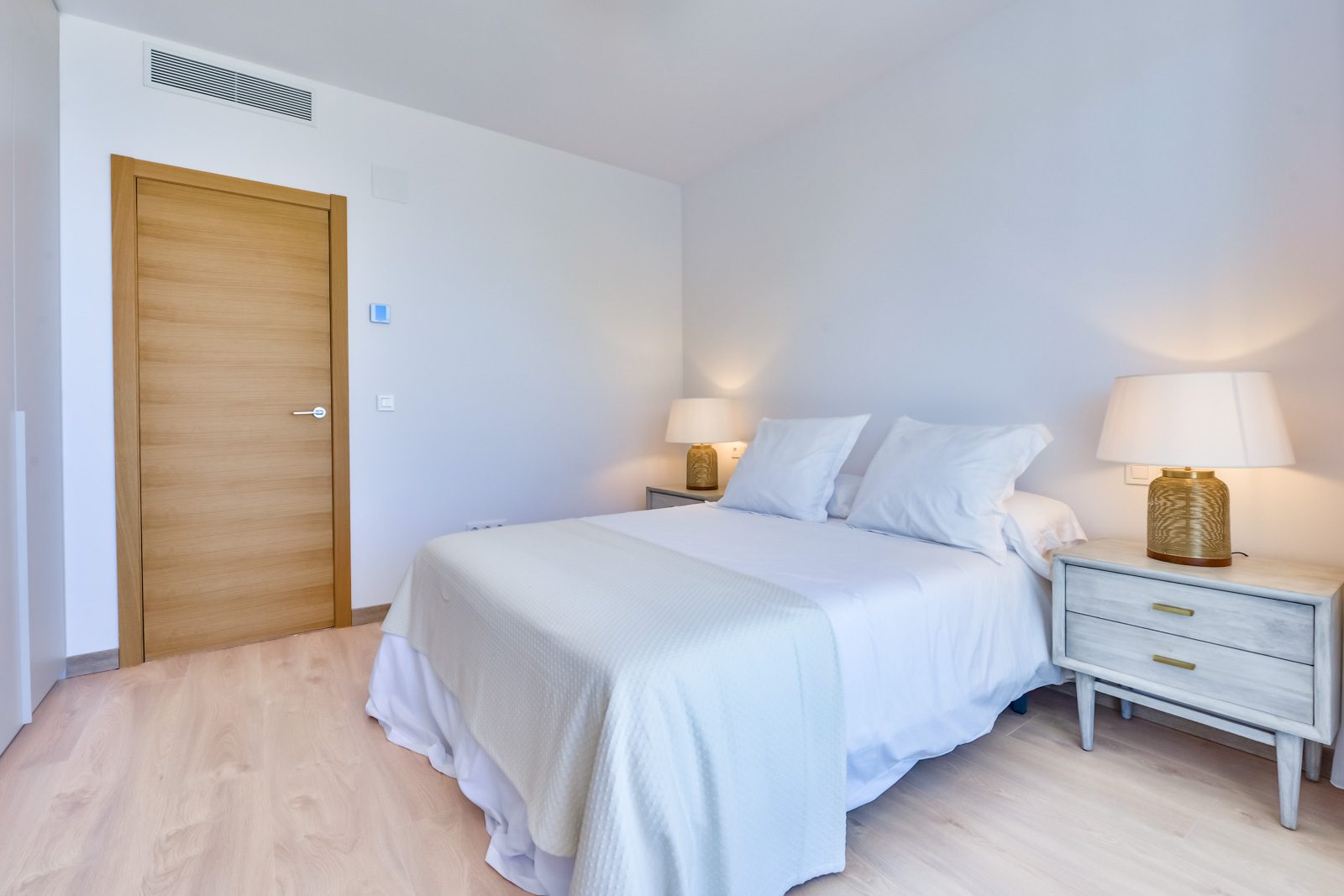 A bright bedroom with a wooden door and bedside lamps in a 3-bedroom villa in Altea - The Estates