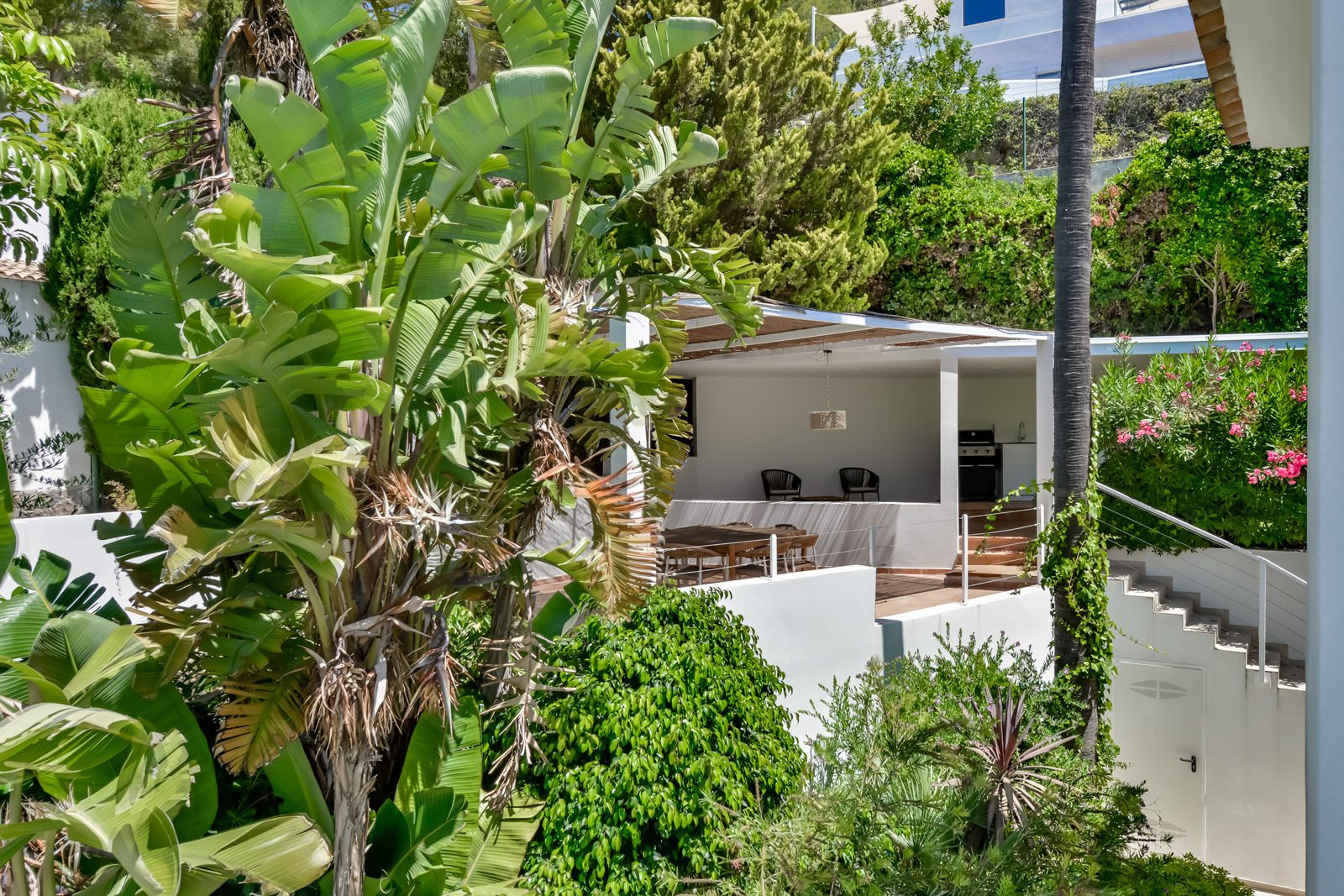 A covered terrace with outdoor dining area surrounded by lush tropical foliage - The Estates