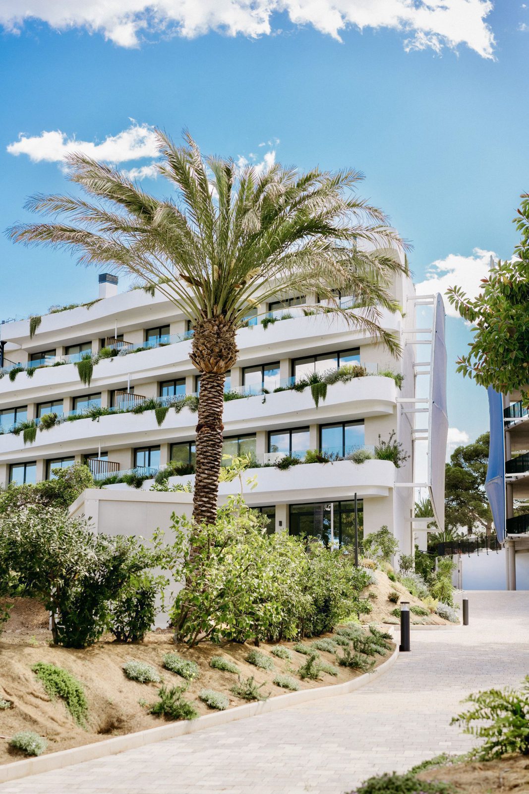A view of a modern apartment building with palm trees and sea views - The Estates