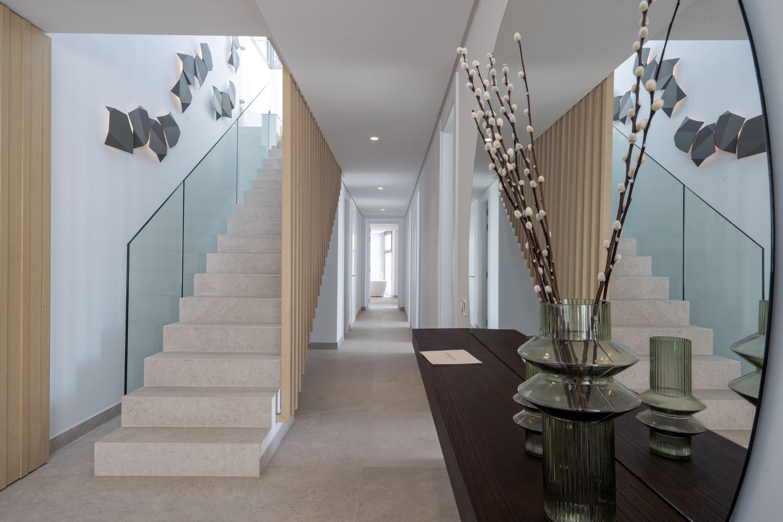 Contemporary hallway with glass staircase, mirrored wall and decorative vases of a 4-bedroom penthouse in Málaga - The Estates