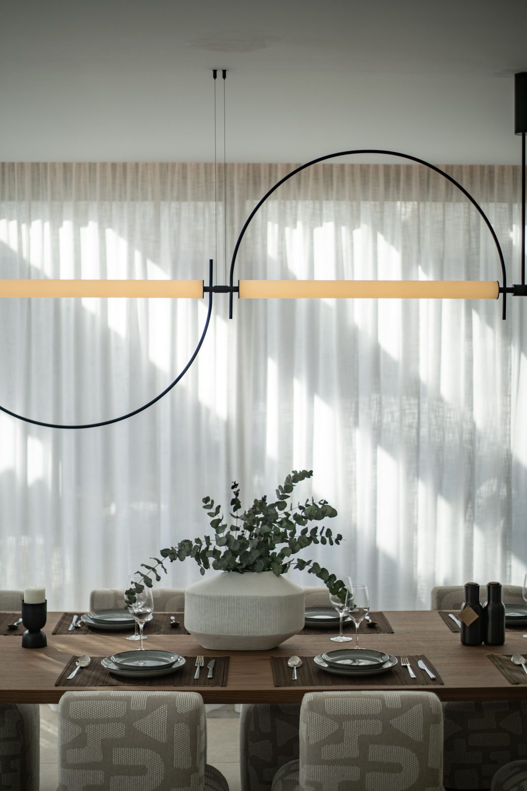 Elegant dining room with set table, sculptural pendant light and sheer curtains of a 4-bedroom penthouse in Málaga - The Estates