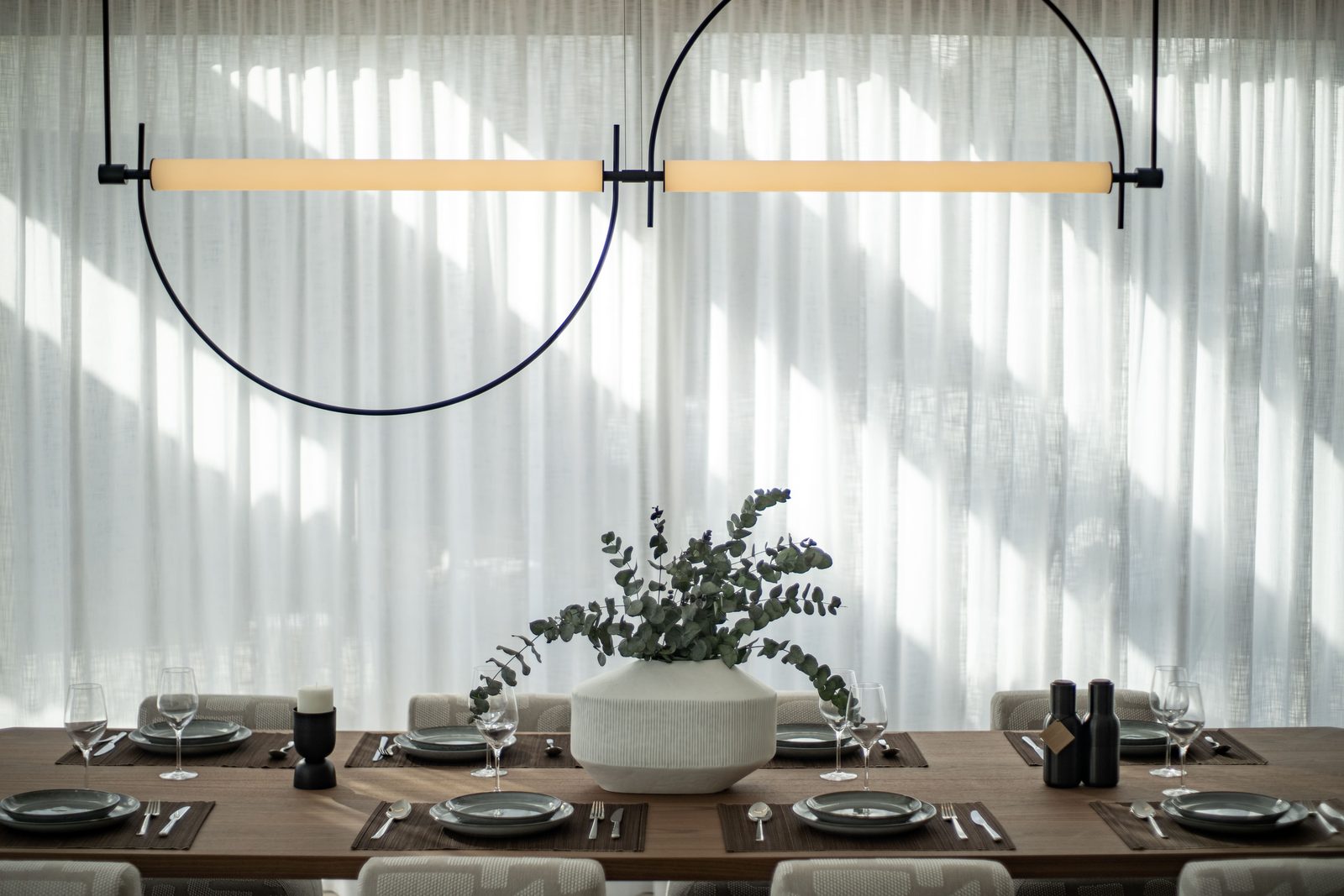 Elegant dining room with a set table, sculptural pendant light and vase of greenery of a 4