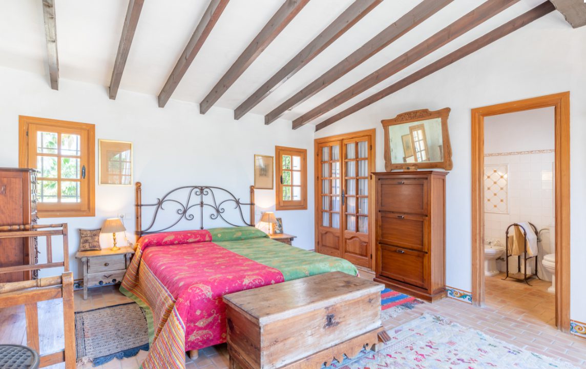 A bright bedroom with wooden beams and a wrought-iron bed in an 8-bedroom finca in Moraira - The Estates