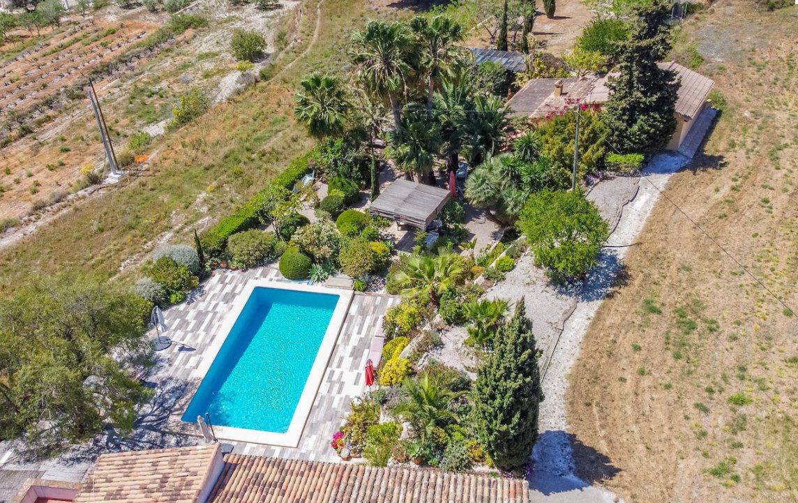 An aerial view of the lush gardens and swimming pool of an 8-bedroom finca in Moraira - The Estates