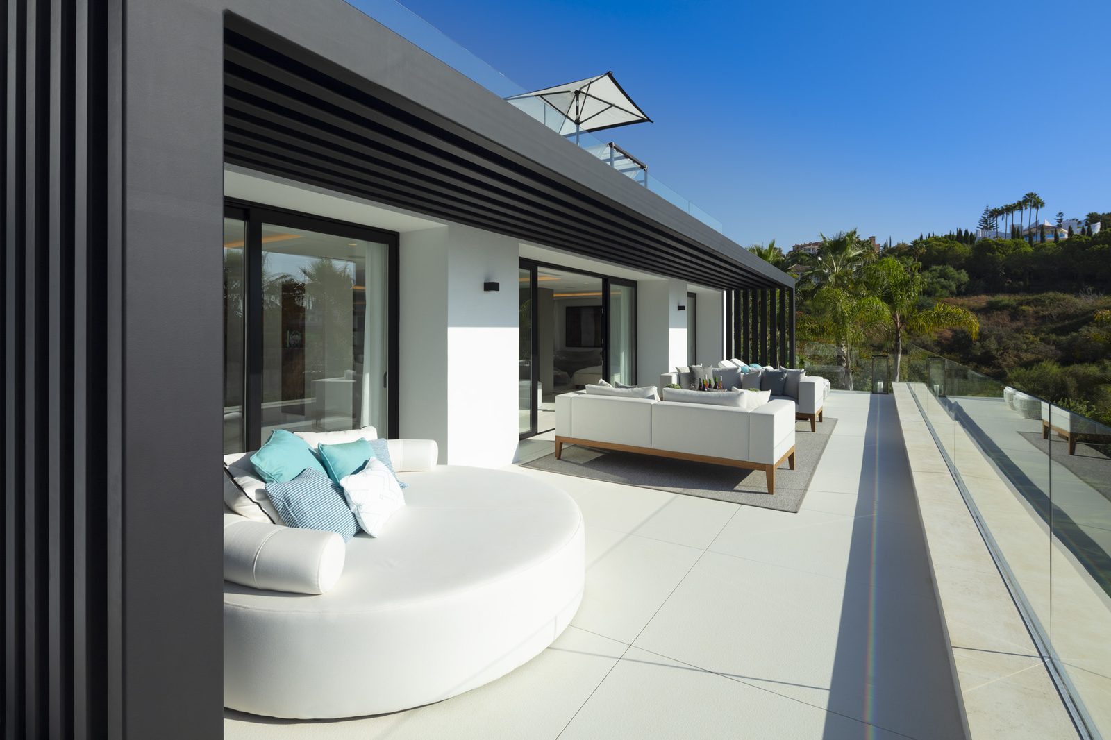 Modern villa terrace with outdoor seating, glass railings and hillside views in Marbella, Málaga - The Estates