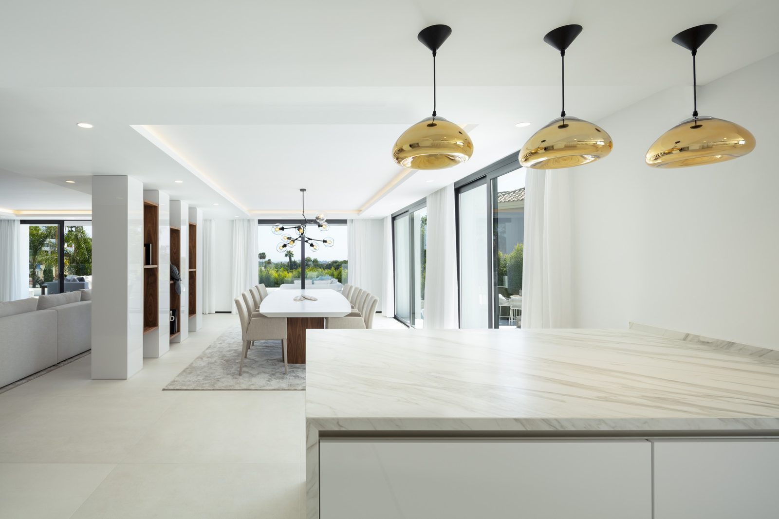 Open-plan kitchen and dining area with marble island, gold pendant lights and golf views in a 5-bedroom villa in Málaga - The Estates