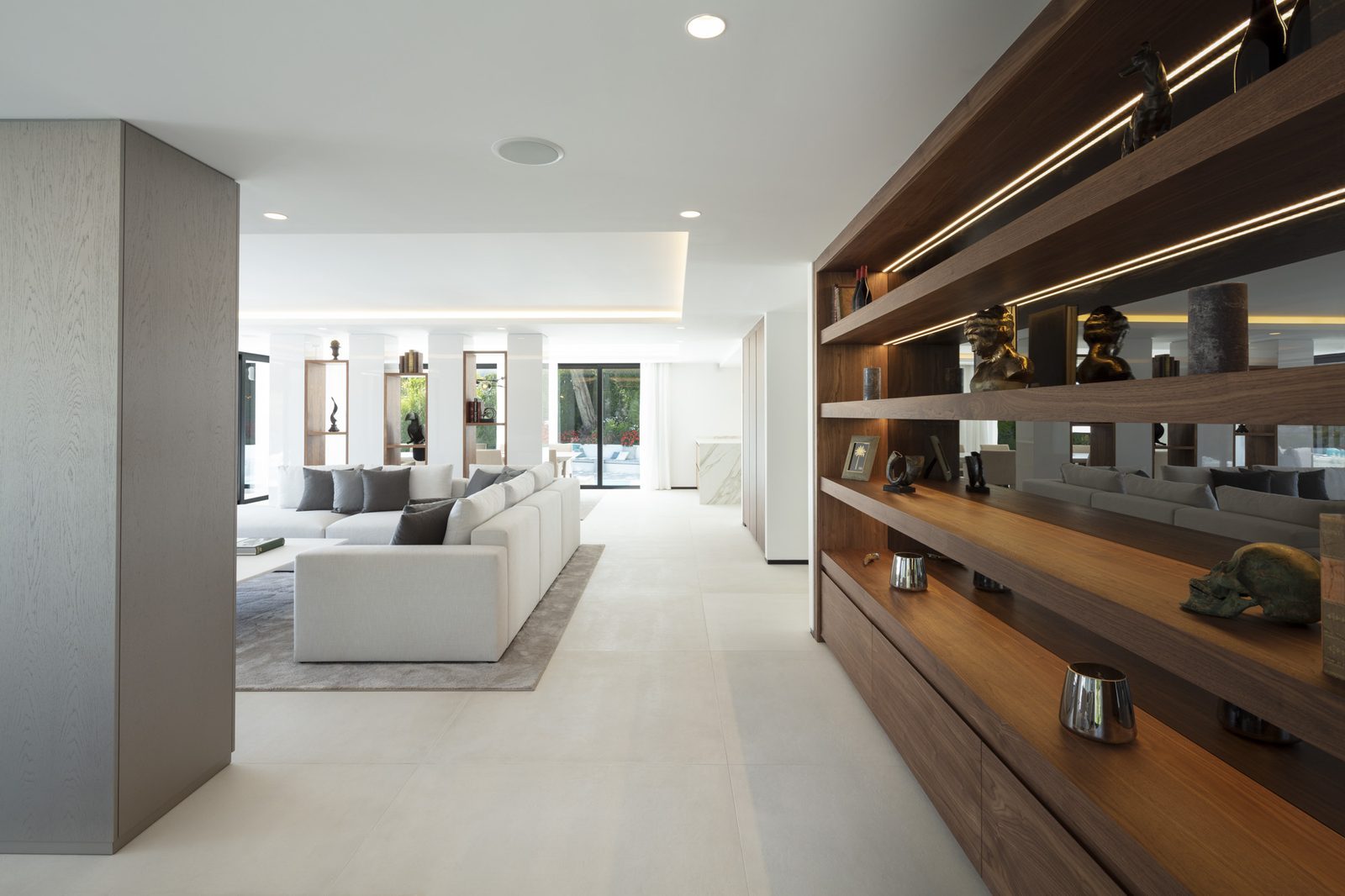 Contemporary living room with illuminated wood shelving and white sofas of a 5-bedroom villa in Málaga - The Estates