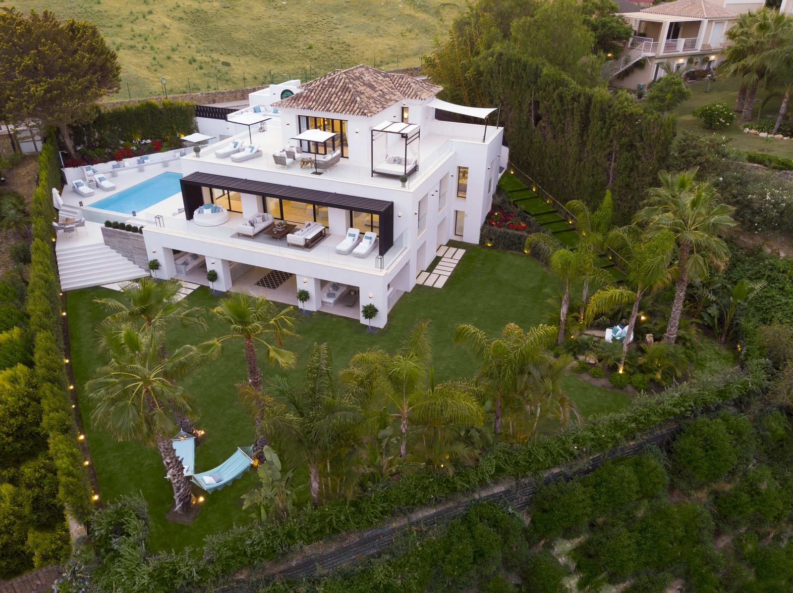 Aerial view of a modern villa with rooftop terraces, pool and palm-filled gardens in Nueva Andalucía, Málaga - The Estates