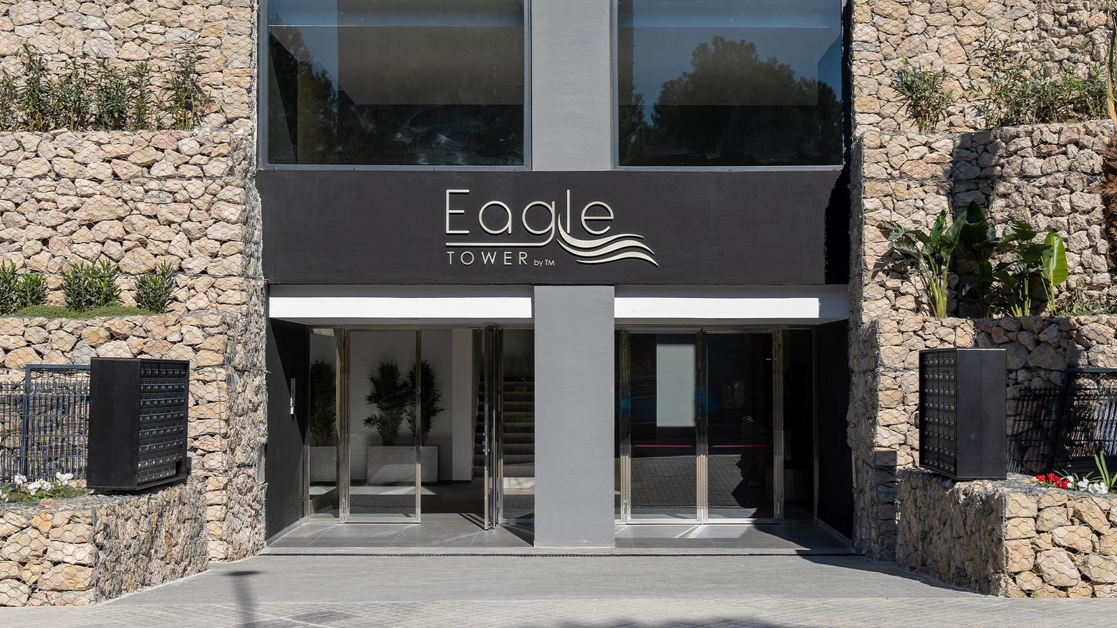 Modern Eagle Tower apartment entrance with stone walls, glass doors and landscaped surrounds in Benidorm - The Estates