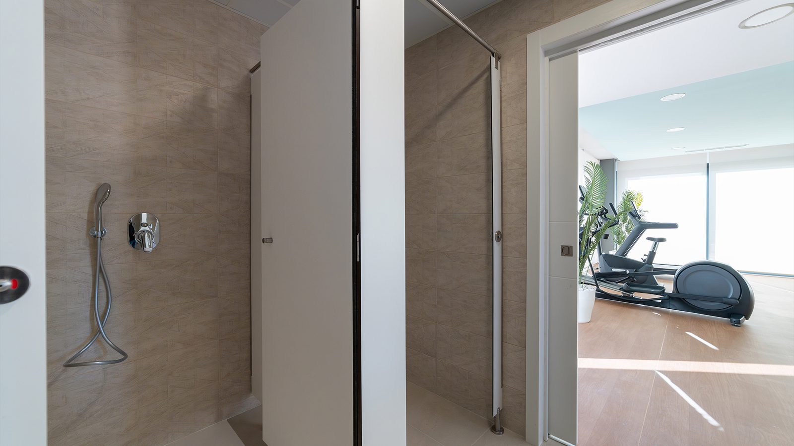 Modern tiled bathroom with walk-in shower and gym equipment visible through the doorway in a 2-bedroom apartment in Benidorm - The Estates