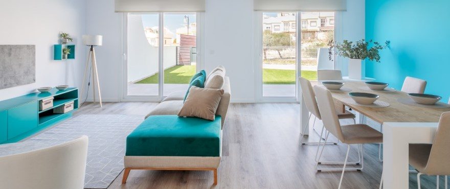 Bright open-plan living and dining room with turquoise sofa, contemporary furnishings and garden views in a 3-bedroom townhouse in Finestrat - The Estates