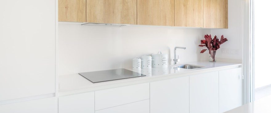 Modern fitted kitchen with wood cabinetry, white units, induction hob and sink in a 3-bedroom townhouse in Finestrat - The Estates