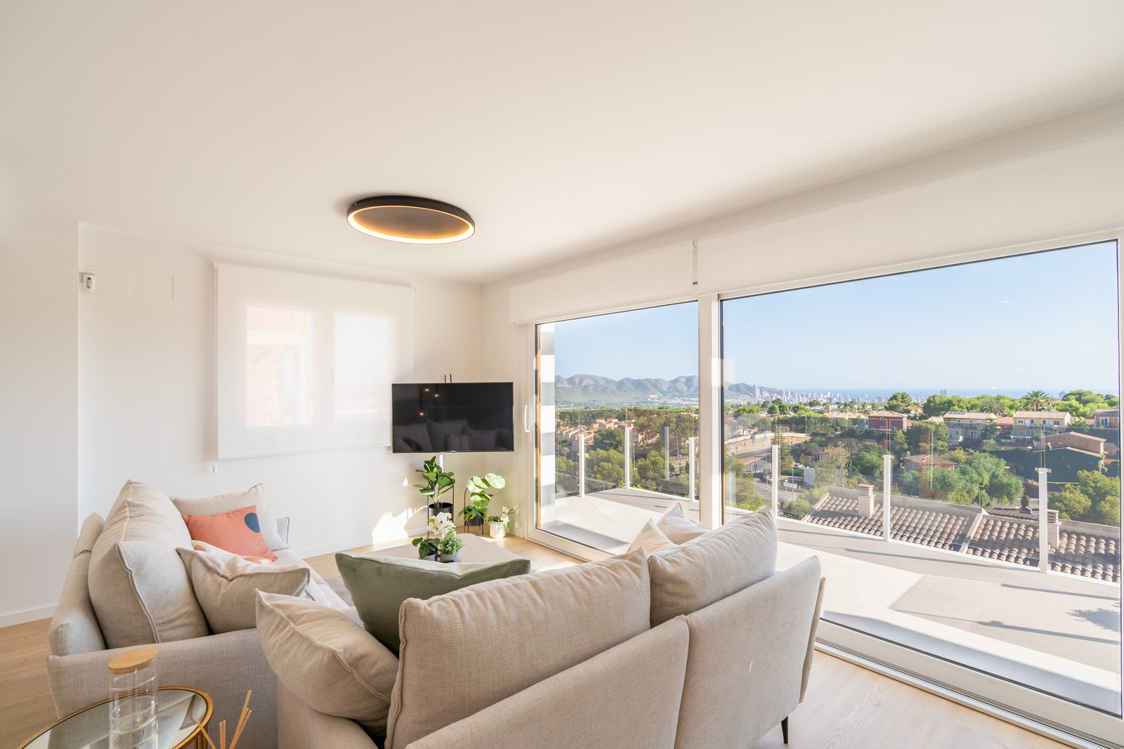 A bright living room with expansive windows showcasing sea and city views of a 4-bedroom townhouse in La Nucía - The Estates
