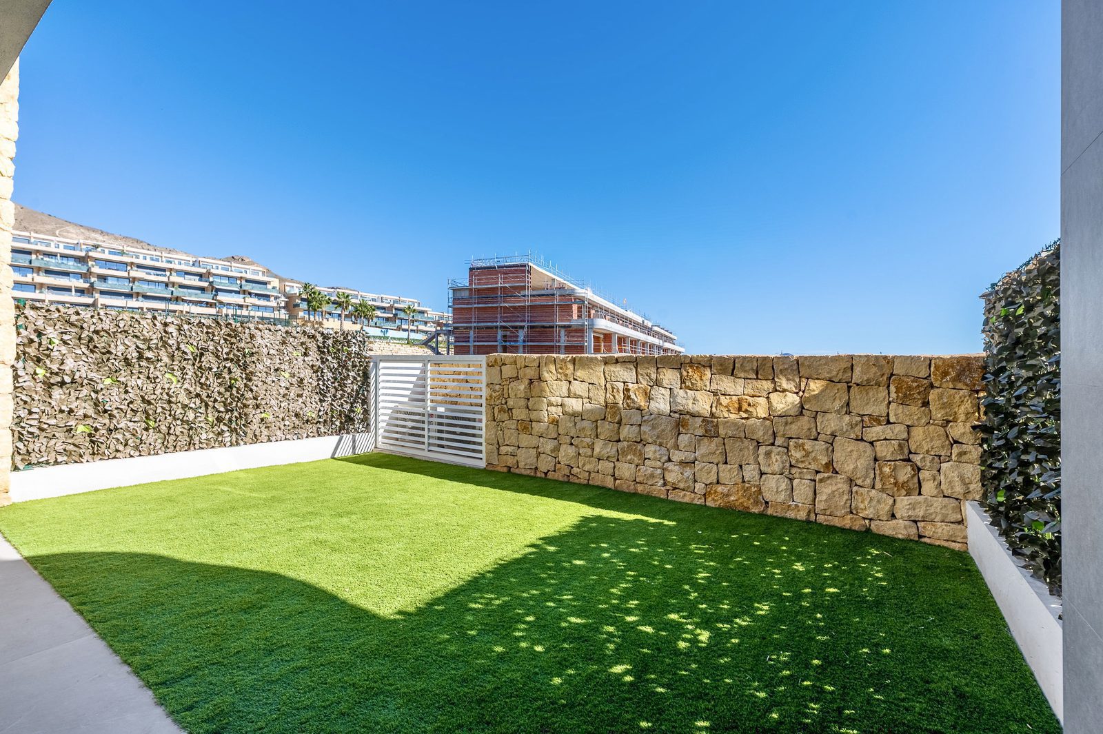 A garden area with artificial grass and stone wall near a 2-bedroom apartment in Finestrat - The Estates