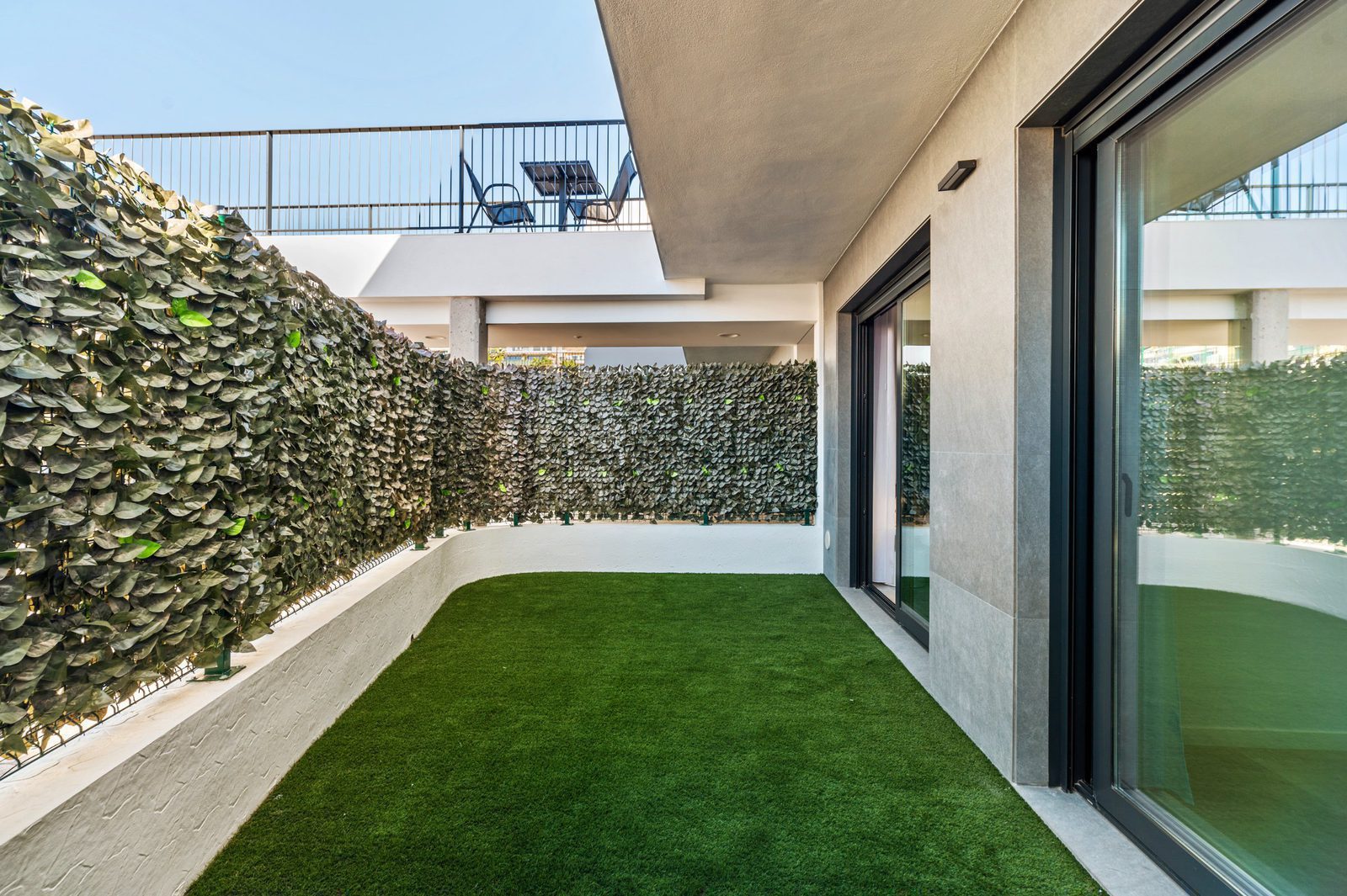 A private balcony with artificial grass and a green hedge, overlooking sea views of a 2-bedroom apartment in Finestrat - The Estates
