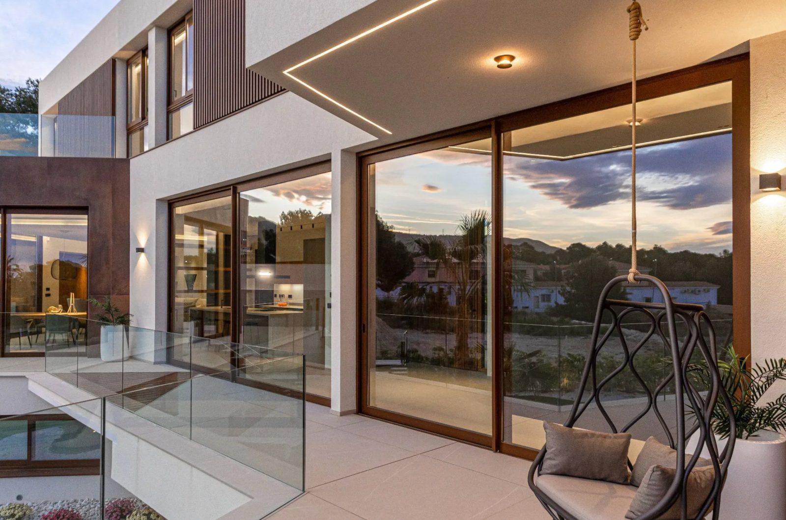 Modern villa exterior with expansive windows and a relaxing swing overlooking sea views - The Estates