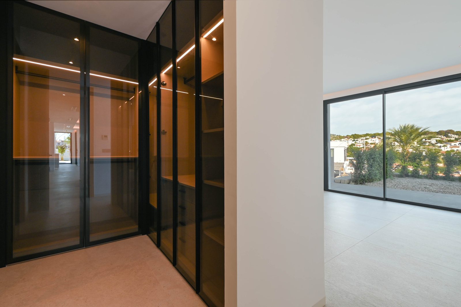 Modern villa interior with illuminated glass-fronted wardrobes and large windows overlooking the landscape, in La Fustera, Benissa - The Estates