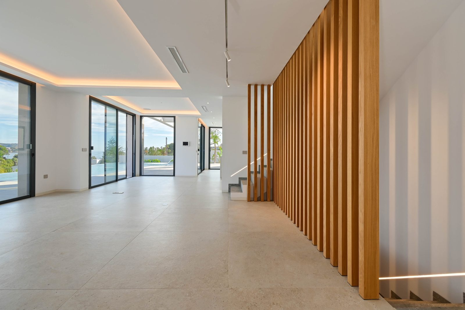 Modern open-plan interior with wood-panelled staircase, floor-to-ceiling windows, pool and sea views of a 4-bedroom villa in Benissa - The Estates