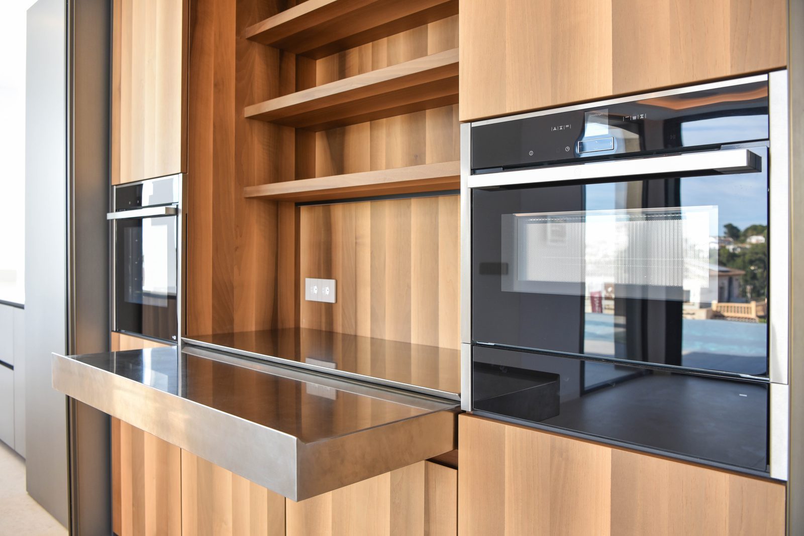 Modern kitchen with wood cabinetry, open shelving and built-in ovens of a 4-bedroom villa in Benissa - The Estates