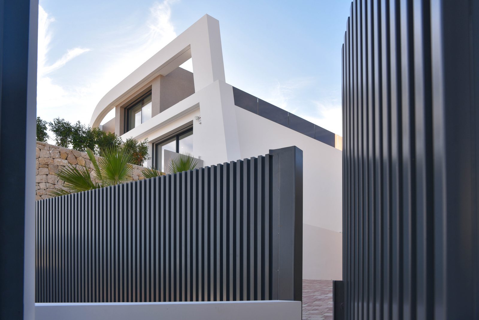 Modern villa exterior with white façades, dark slatted fencing and palm landscaping in Benissa - The Estates