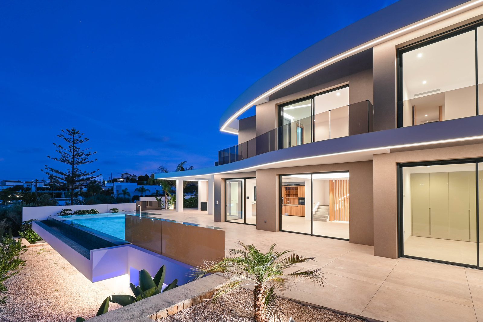 Modern villa exterior with illuminated infinity pool and terraces at dusk in La Fustera, Benissa - The Estates
