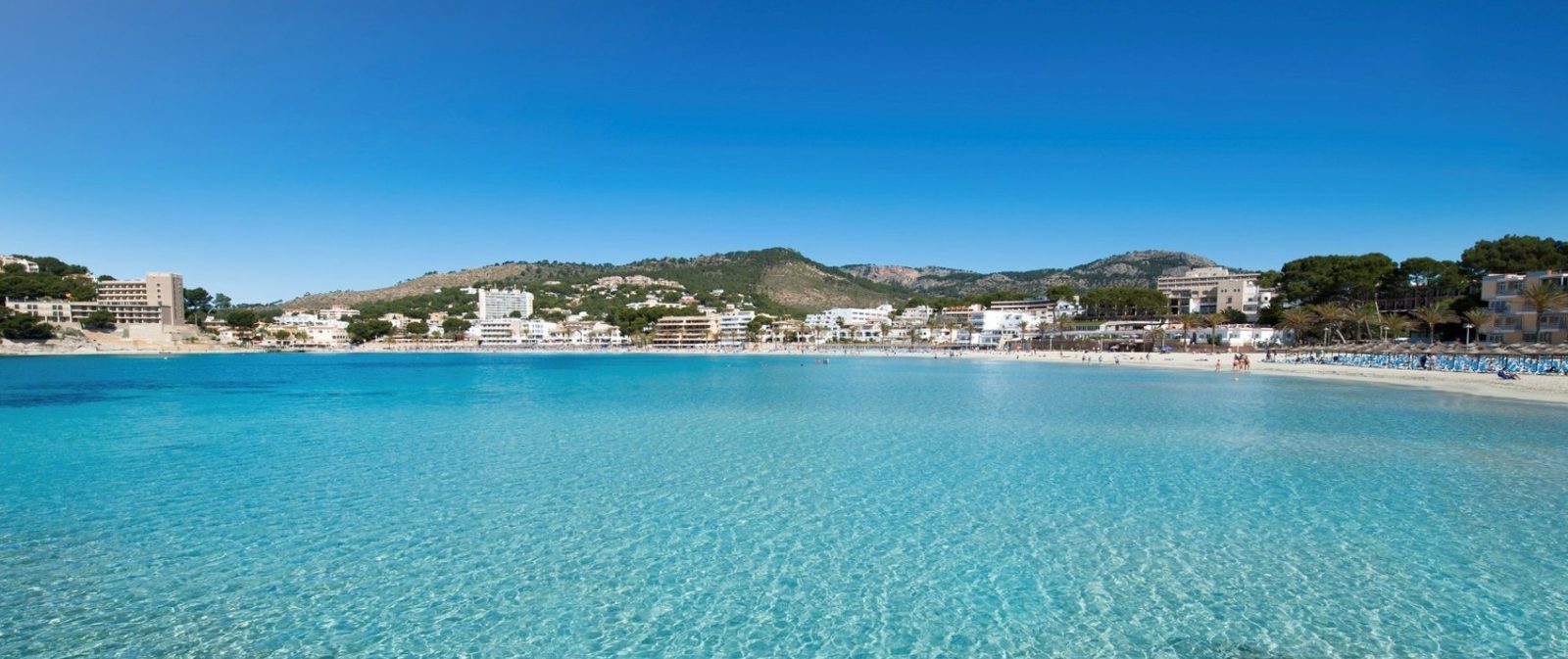 Panoramic view of a turquoise bay, sandy beach and mountain-lined coast near a 2-bedroom apartment in Calvia - The Estates
