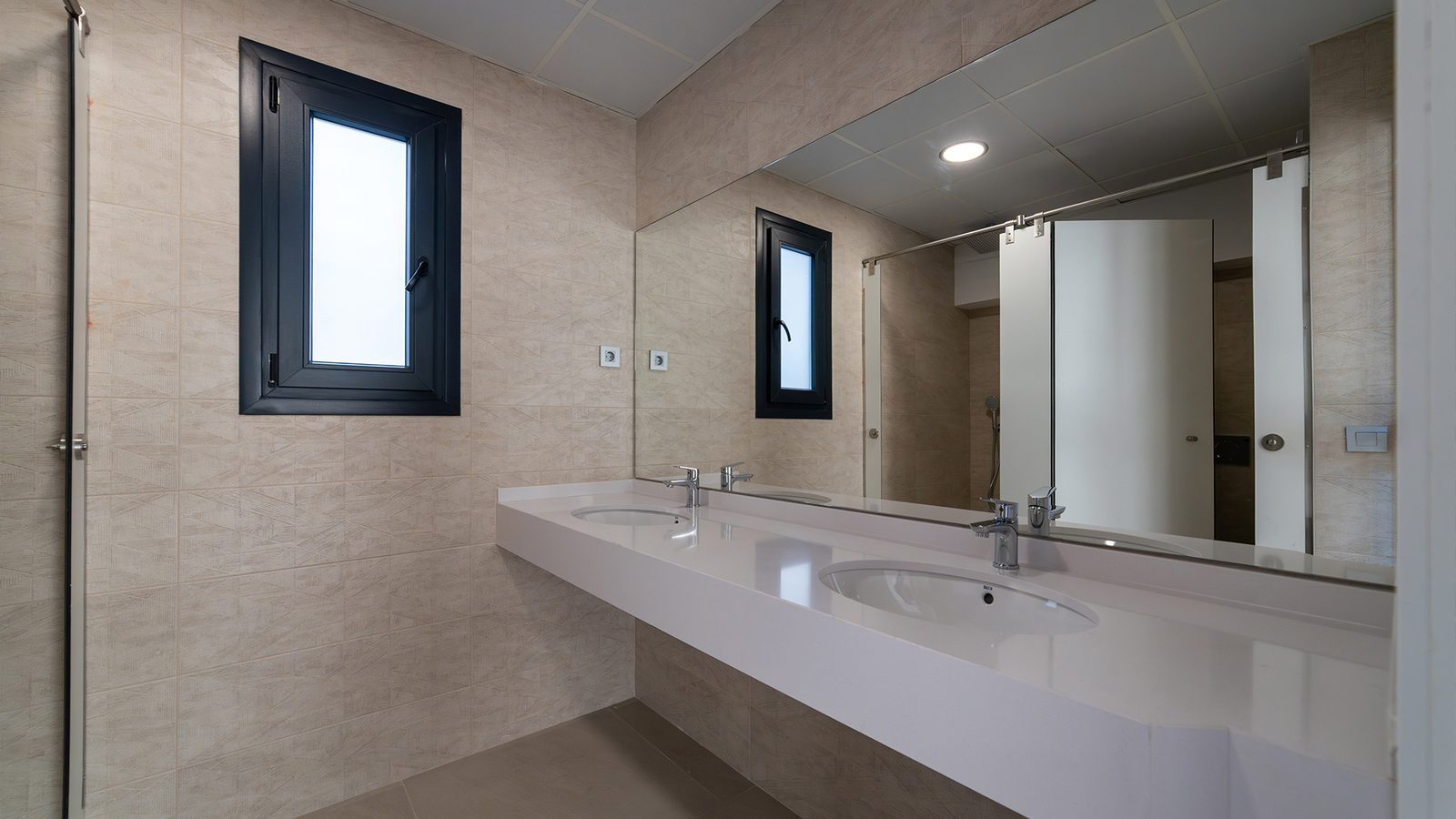 Modern bathroom with twin sinks, large mirror and tiled walls of a 3-bedroom penthouse