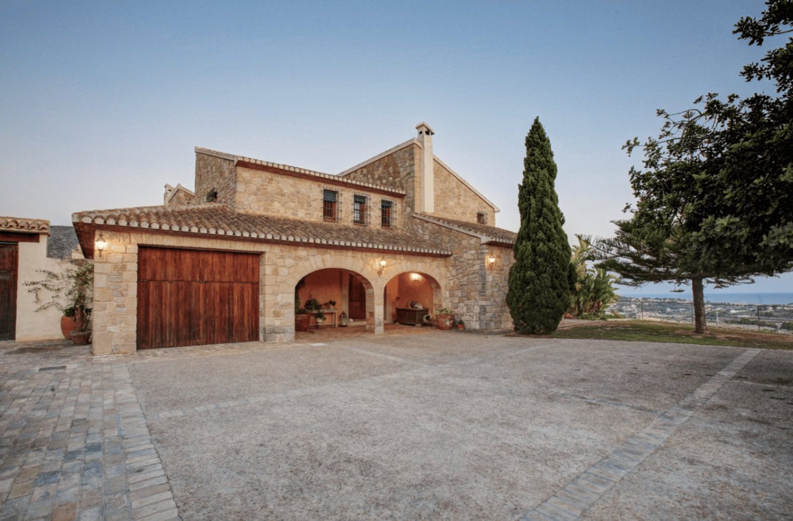 Exterior view of a traditional stone finca with arched entryway and sea views - The Estates
