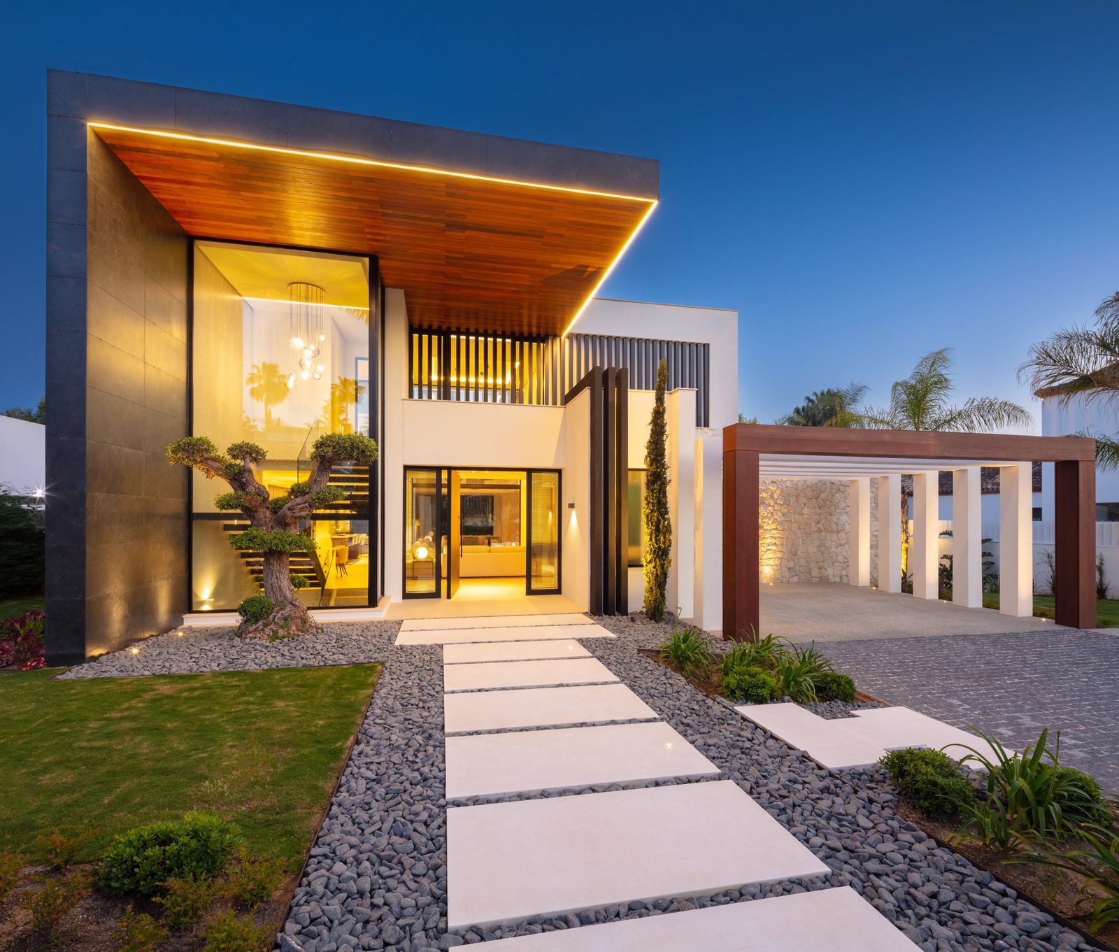 Modern villa exterior with illuminated entrance, landscaped pathway and covered carport of a 5-bedroom villa in Málaga - The Estates