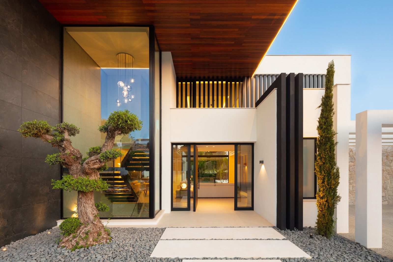 Modern villa entrance with sculpted trees, glass walls and illuminated
