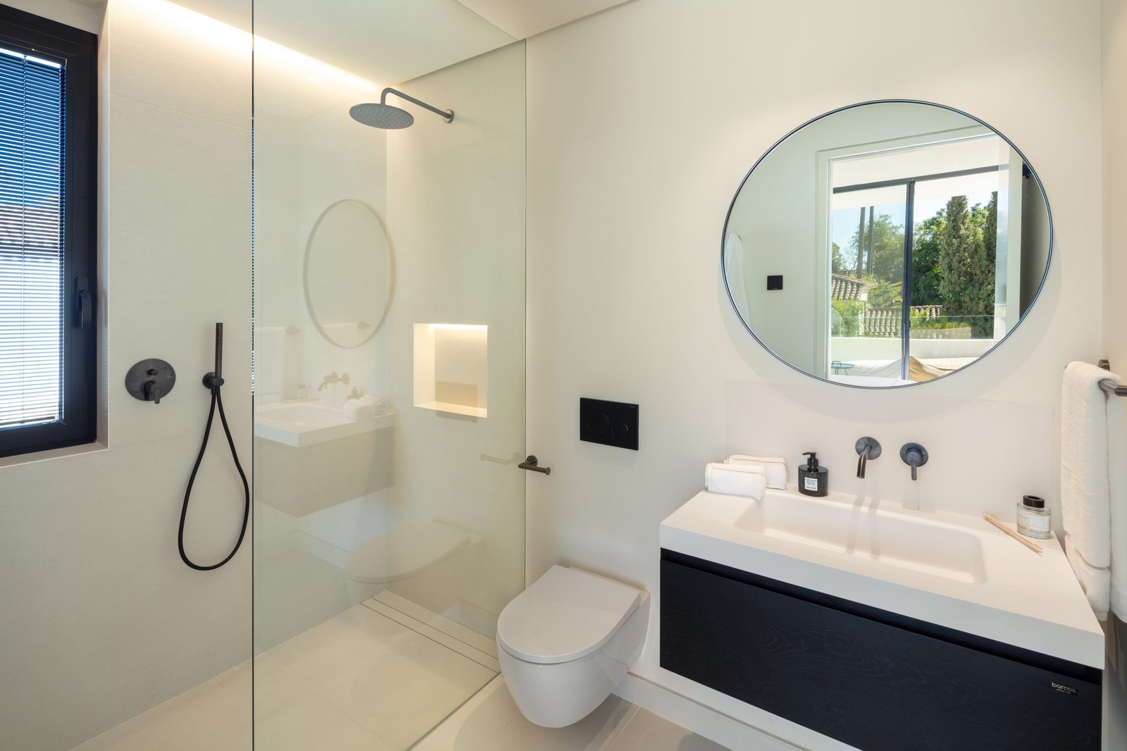 Modern bathroom with walk-in shower, wall-hung toilet, vanity and round mirror in a 5-bedroom villa in Málaga - The Estates