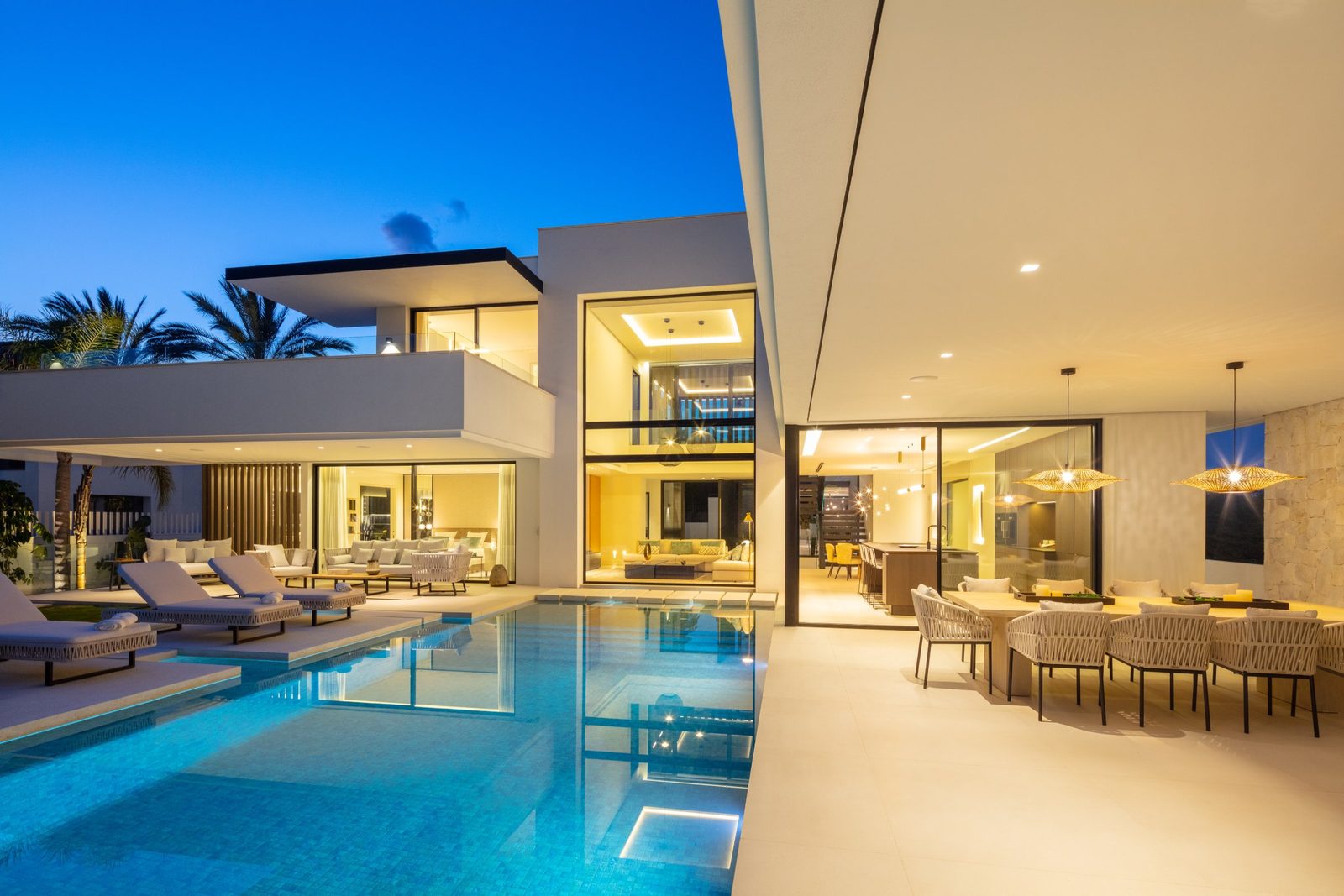 Modern villa with illuminated pool, outdoor lounge and dining area at dusk in Marbella, Málaga - The Estates