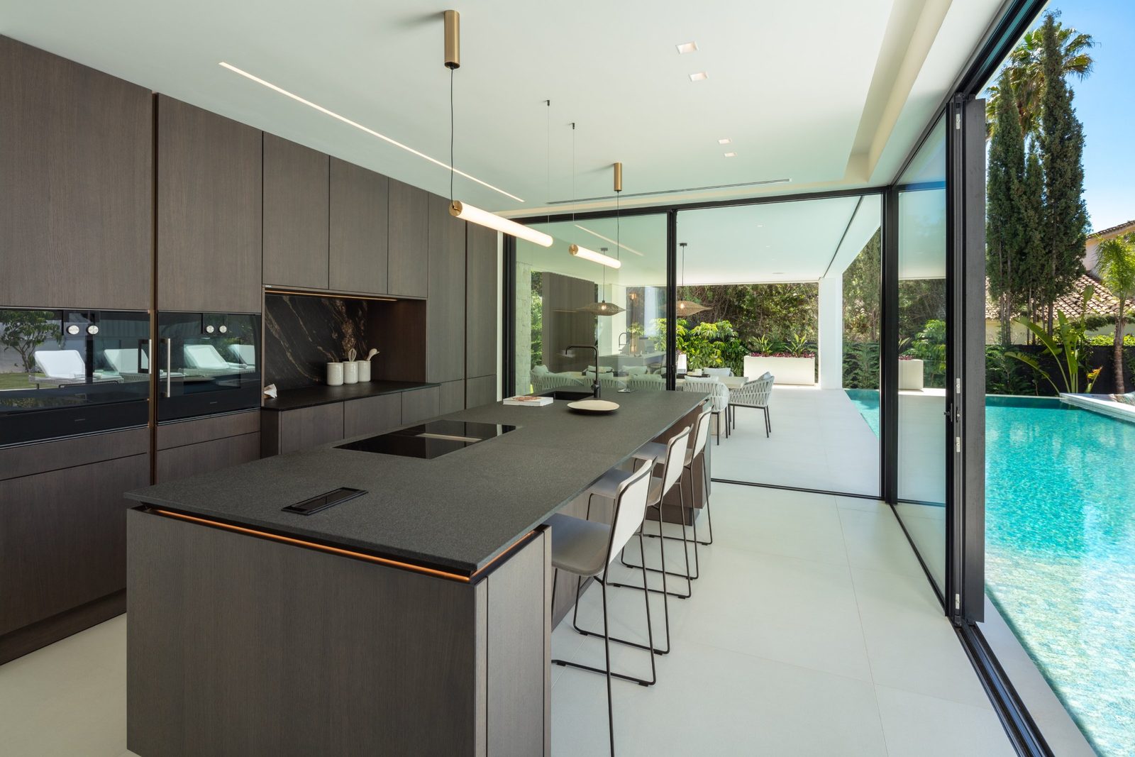 Modern kitchen with central island, bar seating and pool views in a 5-bedroom villa in Málaga - The Estates