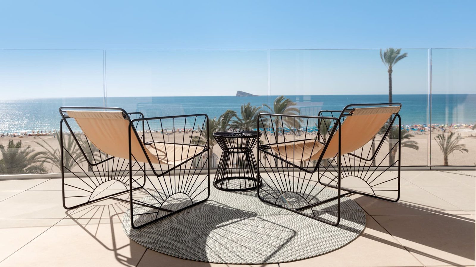 Sea-view terrace with two lounge chairs, a table and panoramic views of Poniente Beach and Benidorm Island in a 2-bedroom apartment in Benidorm - The Estates