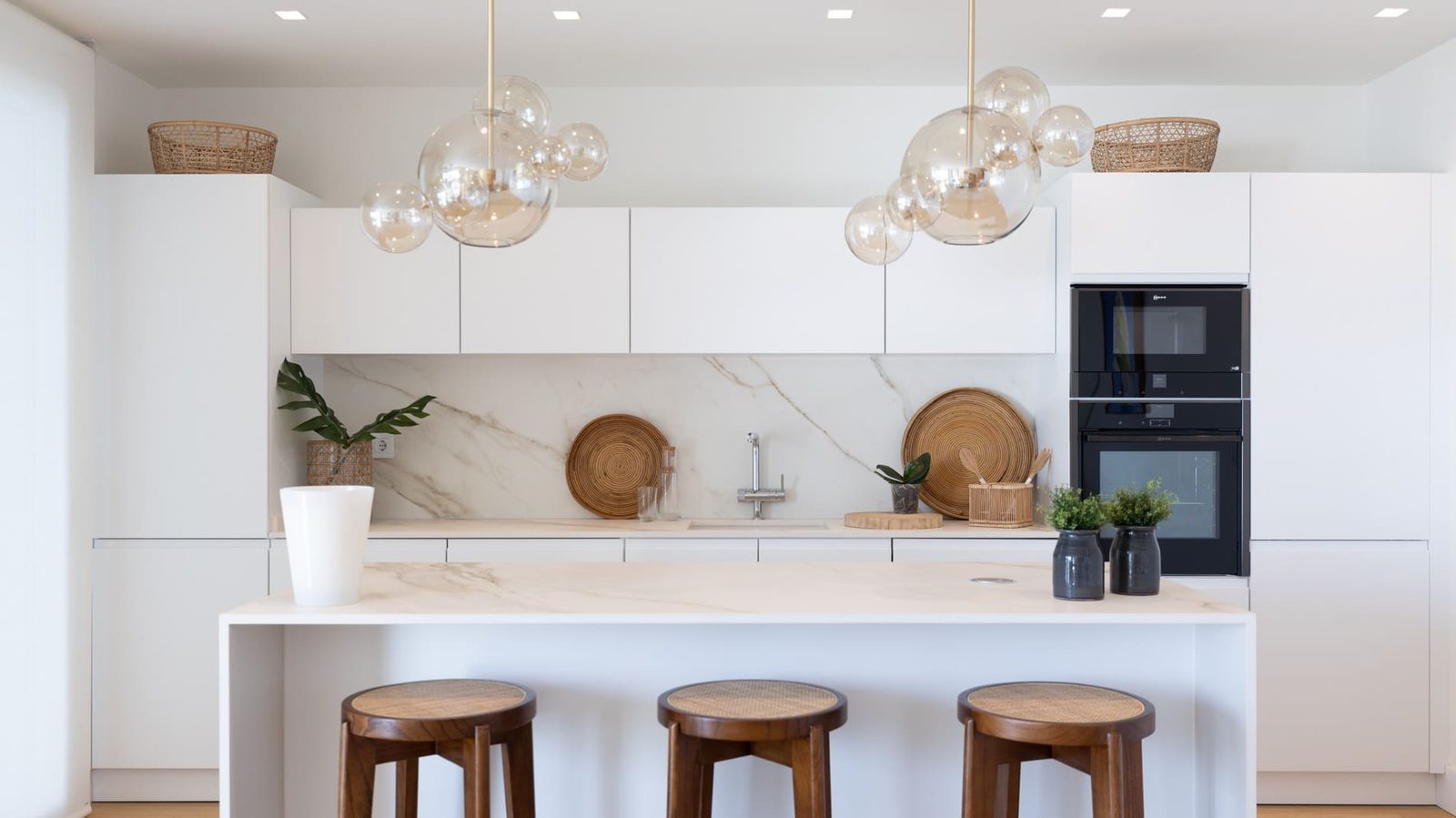 Modern white kitchen with marble island, three wooden stools, built-in appliances and pendant lights in a 2-bedroom apartment in Benidorm - The Estates