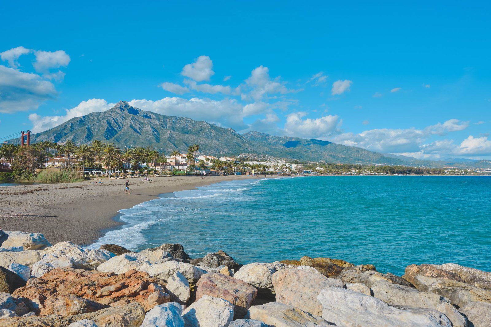 Sandy beach and turquoise sea with palm trees and Sierra Blanca mountains in Costa del Sol - The Estates