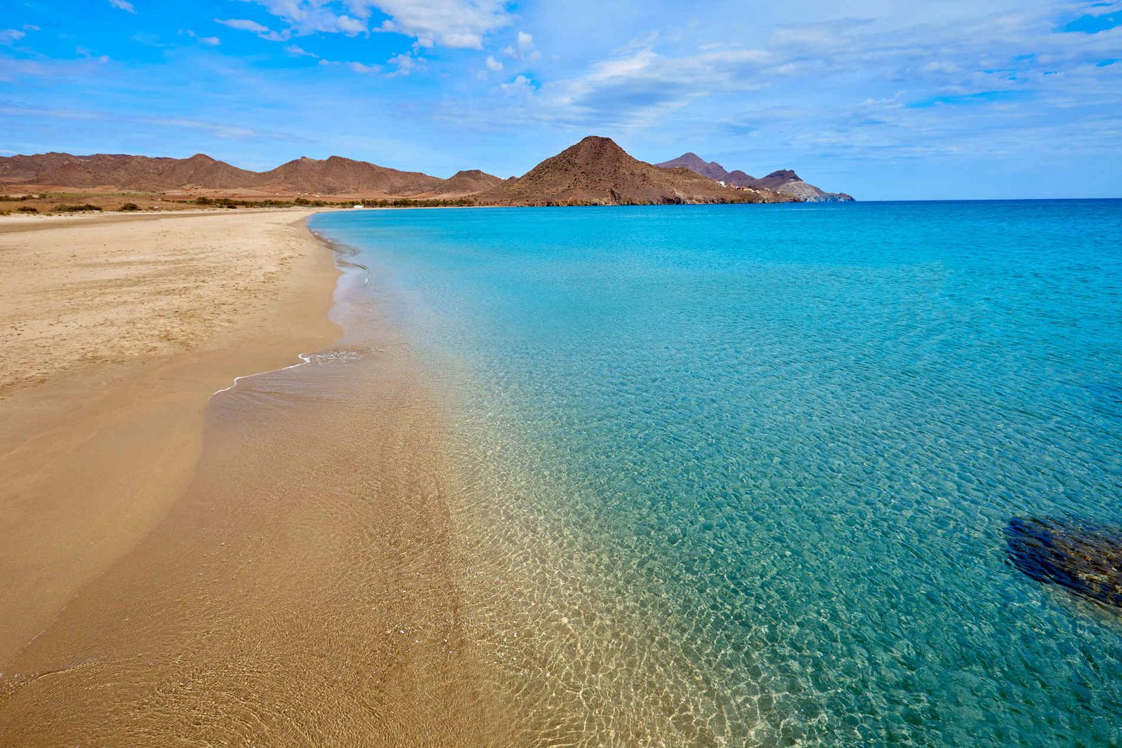 A beautiful beach with clear turquoise water and distant mountains in Costa de Almeria - The Estates